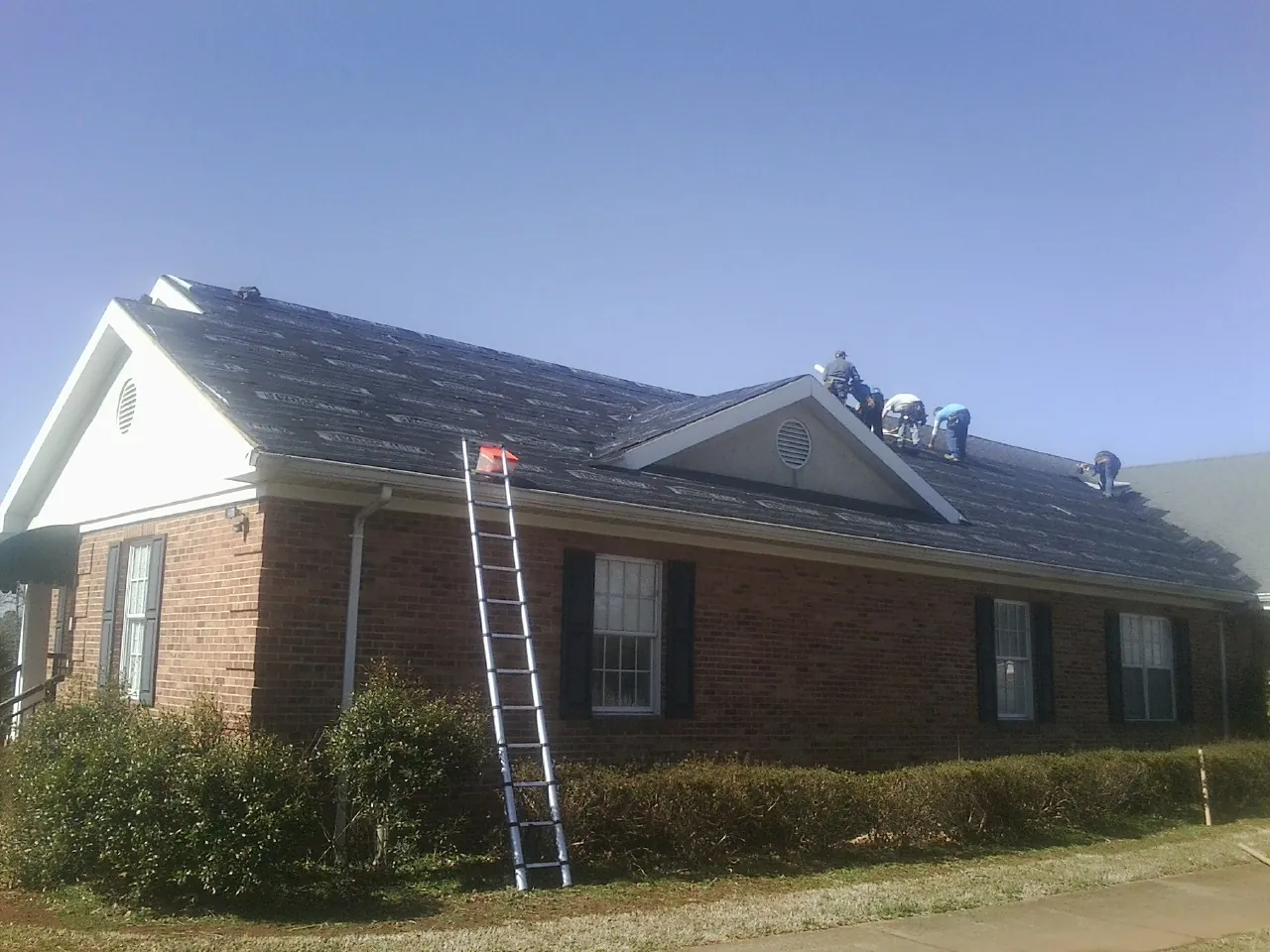 Crew tearing shingles off a brick ranch roof with a ladder set — Emergency Roof Repair work by our crew in Turtle Creek