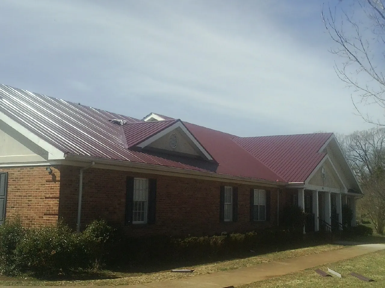 Red metal roof with gabled entries on a long brick building, from a Hail Damage Roof Repair job in Turtle Creek