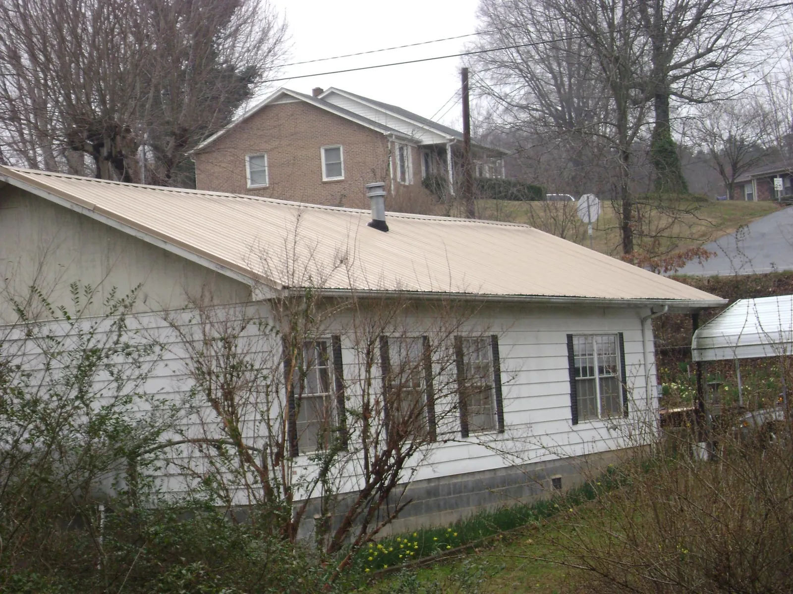 Tan metal roof on a white sided house set into a hillside — Commercial Roofing by Roofing Brothers in Turtle Creek